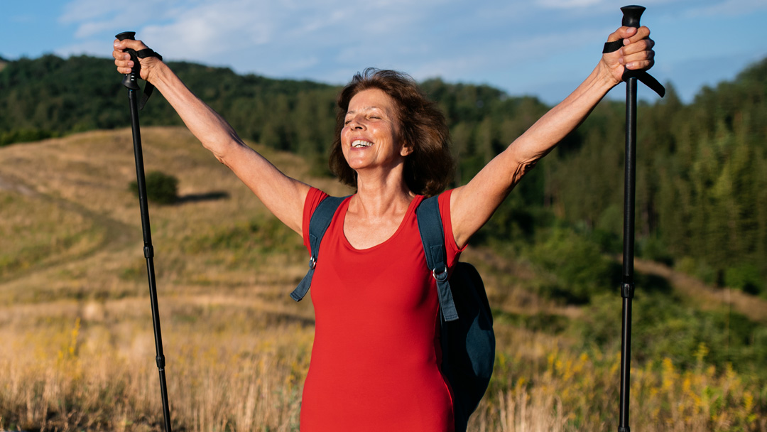 A happy senior woman raising her arms in triumph while hiking with poles, embodying the joy of active aging with joint support.