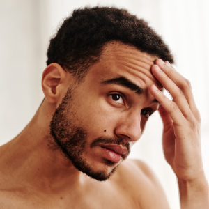 Confidence That Starts with Your Skin A thoughtful young man touching his forehead, representing the personal confidence that comes from healthy, hydrated skin.