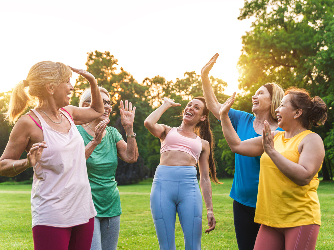 A joyful group of senior women exercising and high-fiving outdoors, highlighting the benefits of community and active aging.