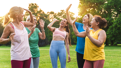 A joyful group of senior women exercising and high-fiving outdoors, highlighting the benefits of community and active aging.