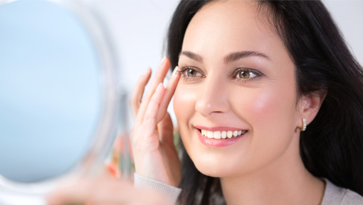 A woman smiling with joy at her reflection while touching her radiant skin, showing the confidence that comes from effective skin support.